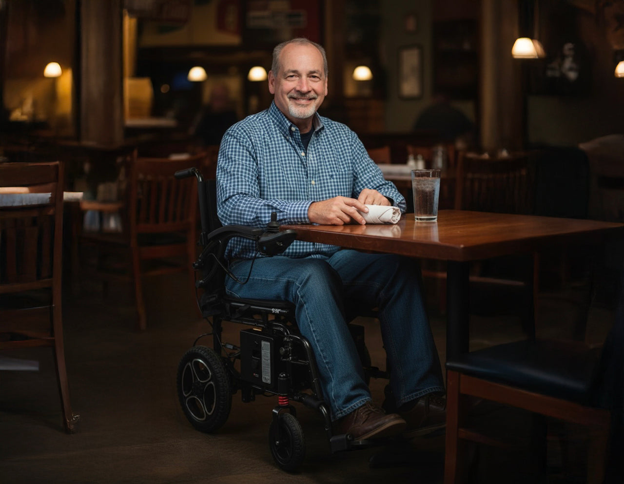 Man in a Journey Air power chair sitting at a table in a restaurant, smiling.