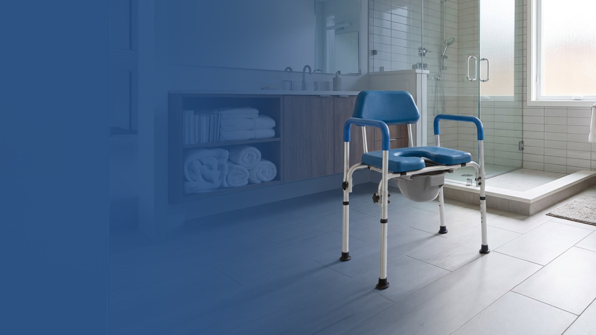 A blue and white medical commode chair is placed on a tiled bathroom floor near a shower, with towels on shelves and sunlight coming through a frosted window.