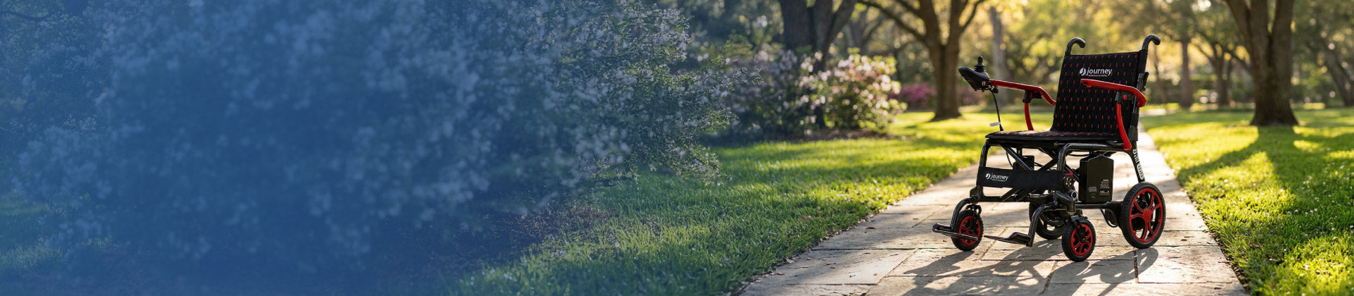 A black and red electric Journey Air Elite is parked on a paved path in a sunny park with green grass and trees in the background.