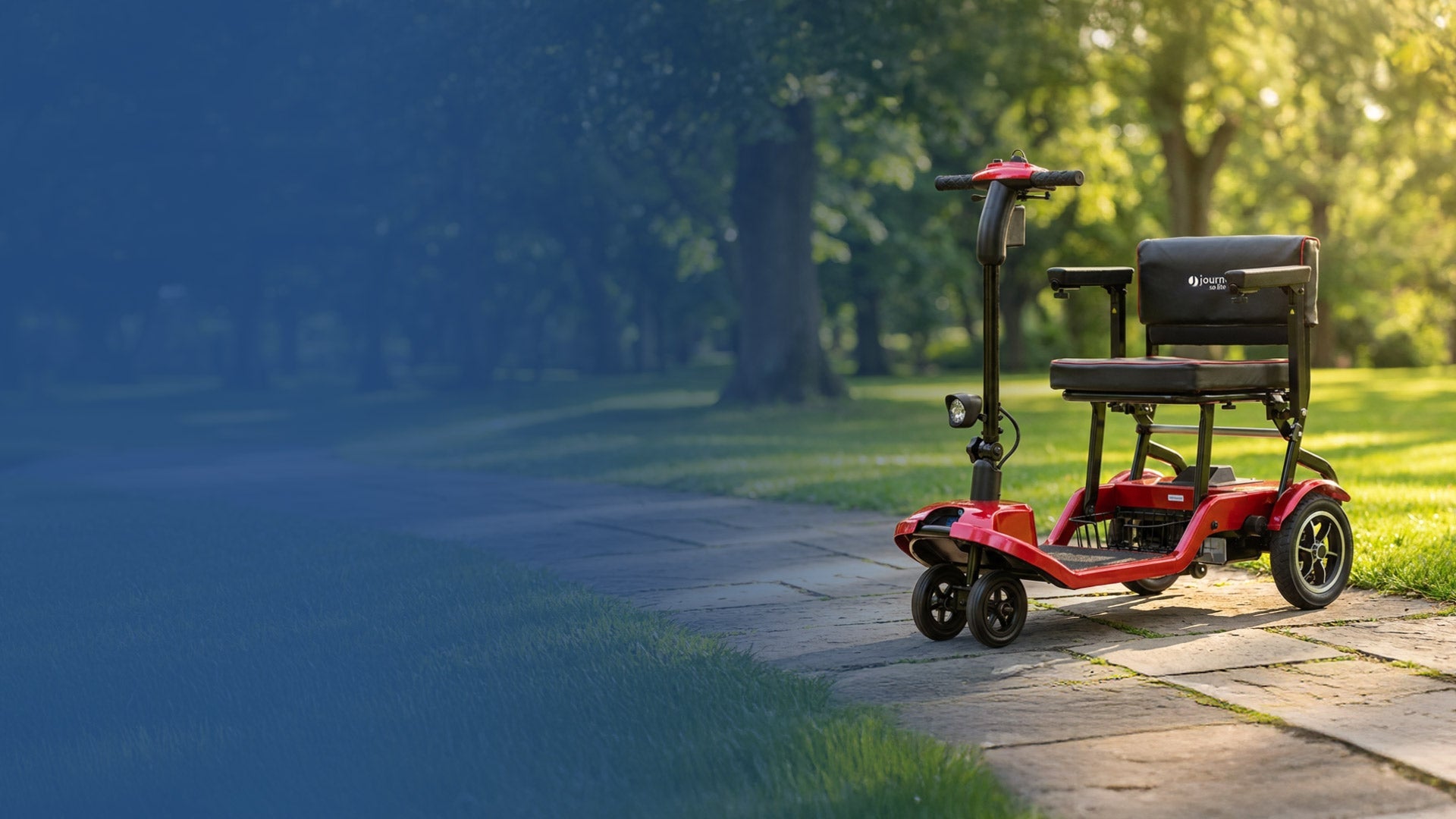A red mobility scooter is parked on a paved path in a green park, with sunlight filtering through the trees. The scooter is empty and facing forward.