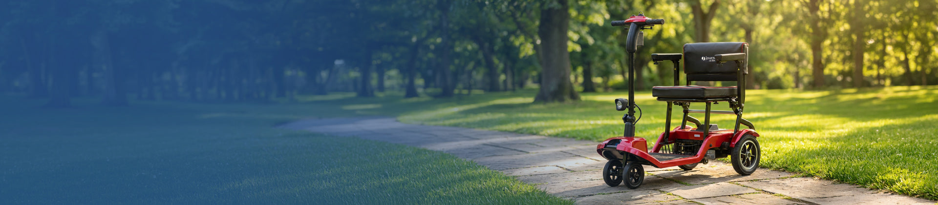 A red mobility scooter is parked on a paved pathway in a green park with trees and sunlight filtering through the leaves.