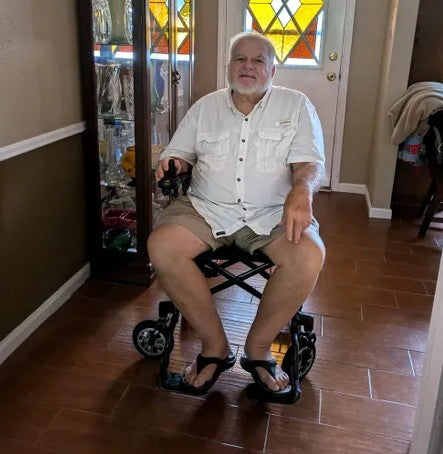 Man sitting in an Air Elite Max powerchair in a home setting with a door and furniture in the background.