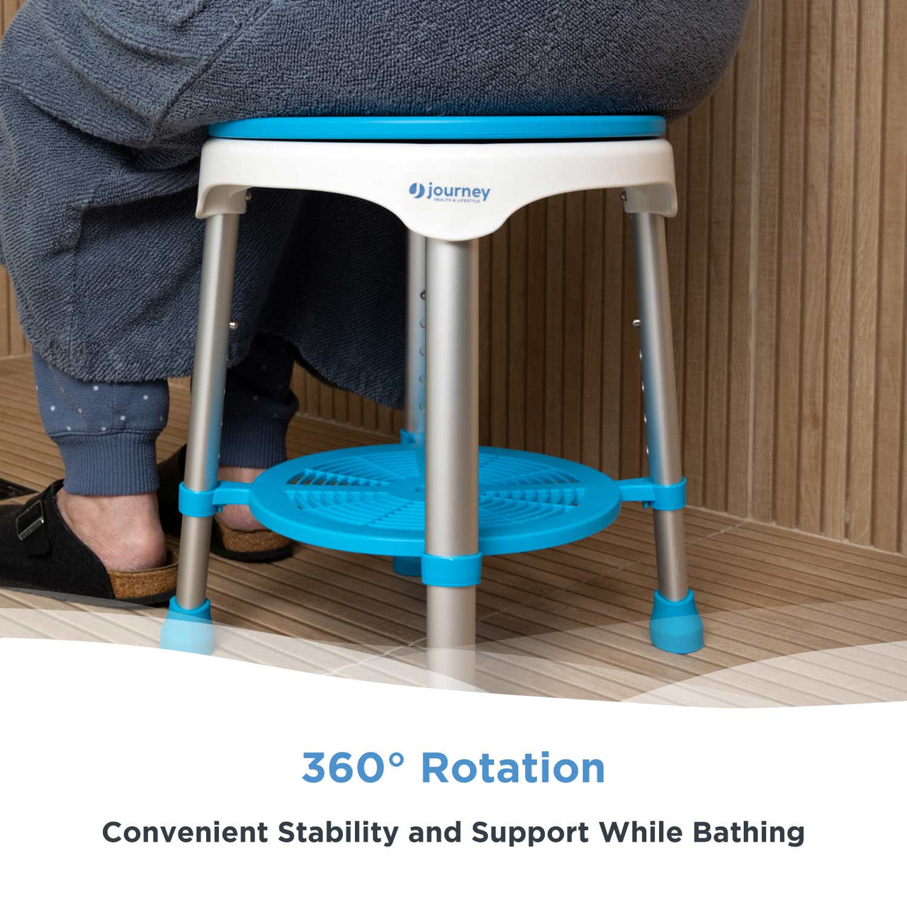 A person in a blue bathrobe sits on the Journey EZ Swivel Shower Stool, a blue and white round seat with 360° rotation, adjustable legs, footrest, non-slip feet, providing stability and support while bathing.