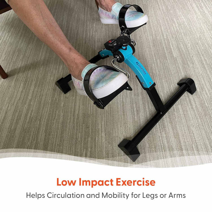 A person pedals a blue Journey Exercise Peddler with a portable design while seated, wearing white sneakers. Text: Low Impact Exercise – Supports Circulation and Mobility for Legs or Arms. Ideal for convenient workouts anywhere.