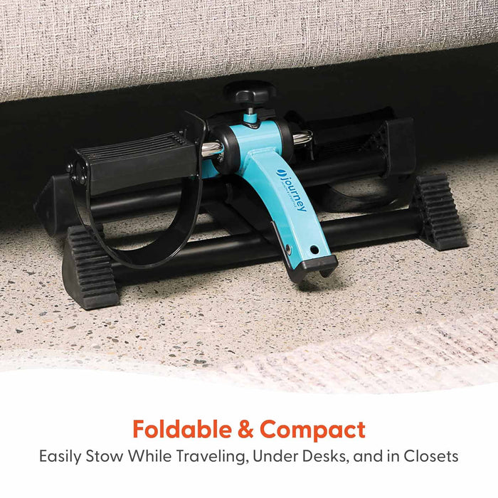The Journey Exercise Peddler, featuring black foot straps and a blue foldable frame, is stored under a couch on a speckled floor. Text: “Foldable & Compact—ideal for low-impact workouts and easy storage or travel.”
