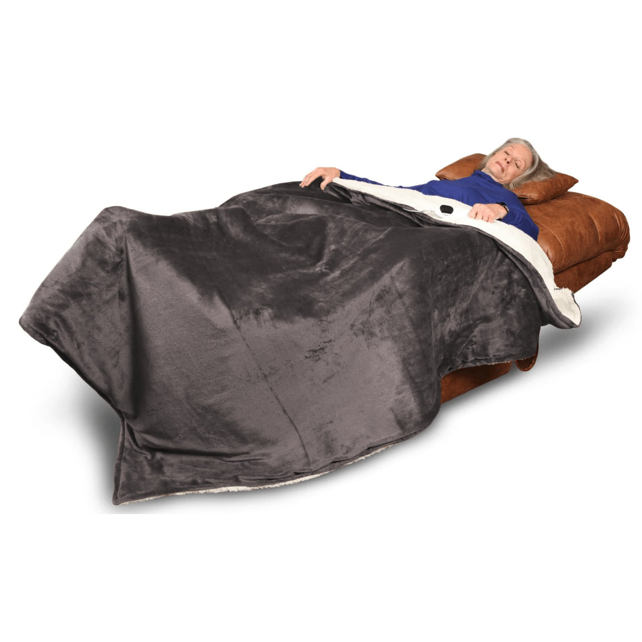An older woman relaxes on a brown recliner, covered with a large gray Journey Companion Heating Blanket, looking comfortable and at ease.