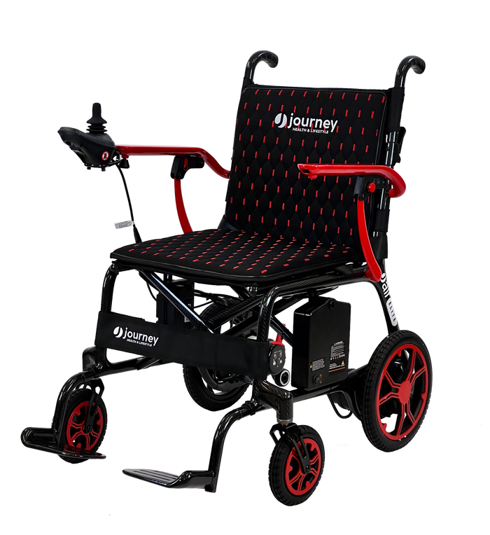 The Journey Air Elite Lightweight Folding Power Chair is a black and red compact wheelchair with joystick controls, cushioned seat and backrest, large rear wheels, small front wheels, footrests, and visible Journey branding.