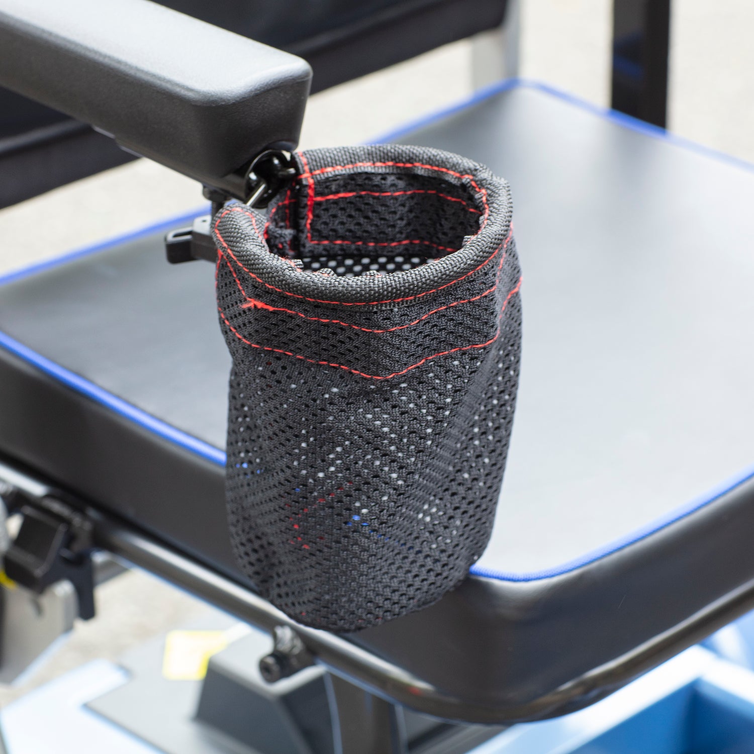 A black mesh cup holder with red stitching is attached to the armrest of the Journey So Lite Folding Power Scooter, positioned beside the seat.