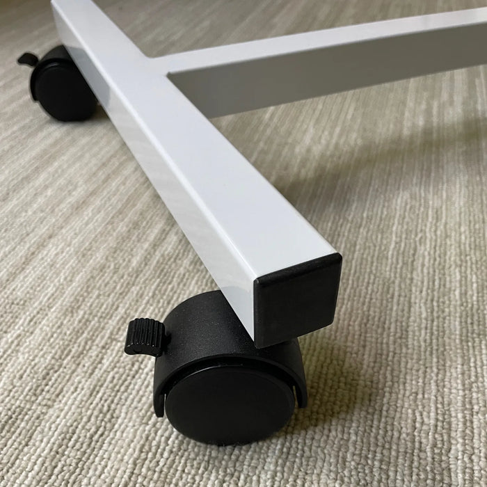 Close-up of the base of the Journey Adjustable Height Overbed Table with white metal legs and black swivel casters on a textured light carpet.