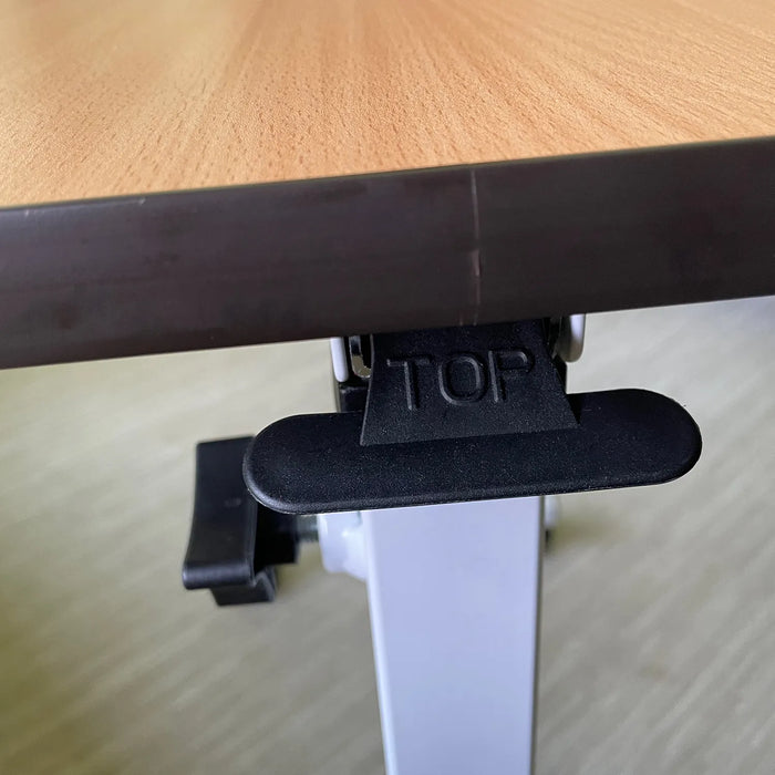 Close-up of the Journey Adjustable Height Overbed Table edge, featuring a black plastic latch labeled TOP under the tabletop, with visible metal support and adjustable mechanism underneath.