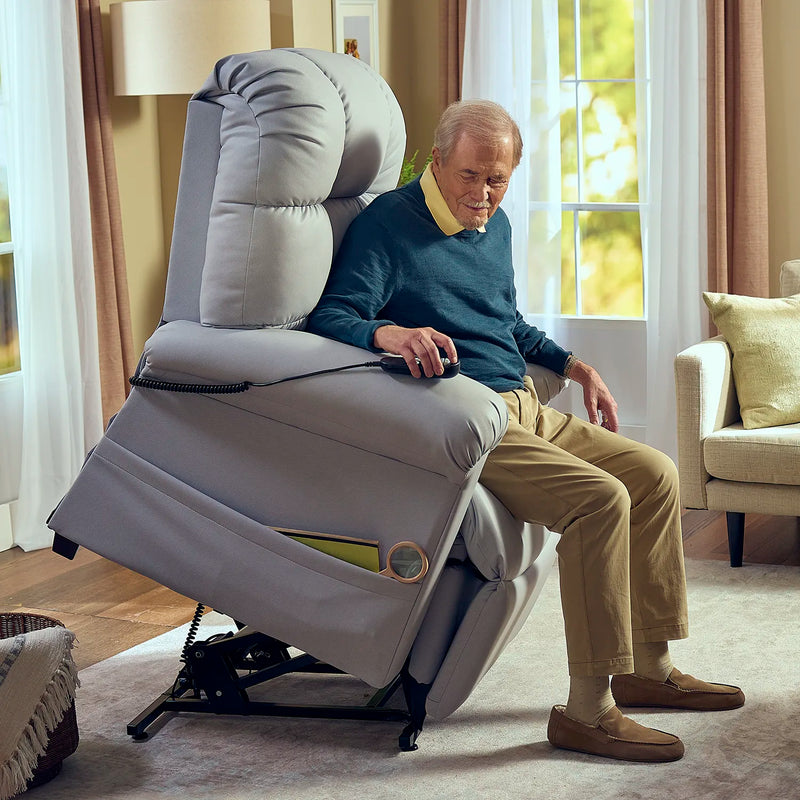 An older man relaxes in a Perfect Sleep Chair & Lift Chair, which features therapeutic heat and massage, as it gently lifts him to his feet in a bright living room with large windows and neutral furniture.