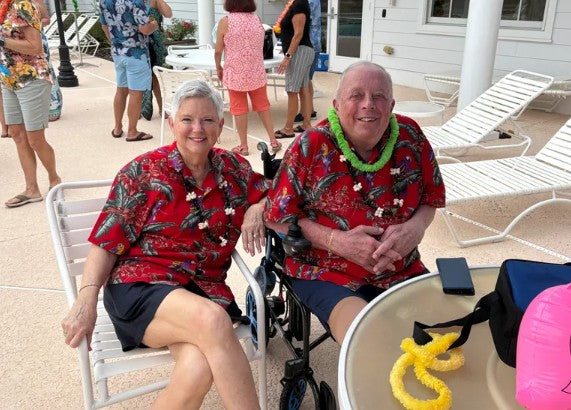 Two people in red Hawaiian shirts sitting by a poolside with others in the background.