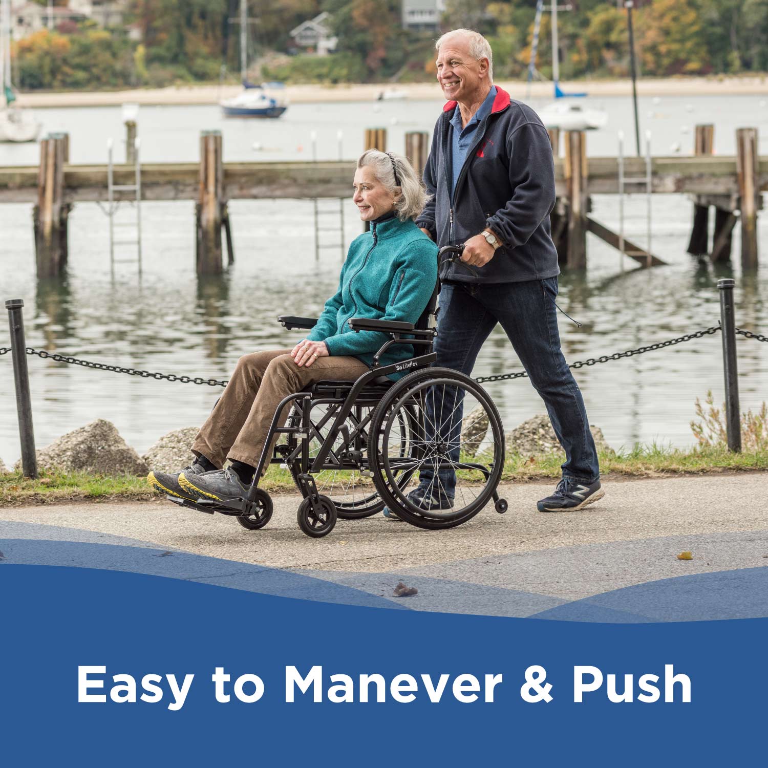 An older man pushes an older woman in a Journey So Lite® C2 Ultra Lightweight Wheelchair along the waterfront. Both are smiling, enjoying the smooth ride. Boats and docks appear in the background. Text reads: Easy to Maneuver & Push.