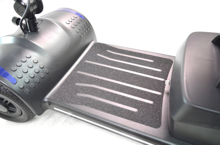 Close-up of the foot platform area of the Journey Adventure Scooter, featuring textured grip strips and part of the wheel and body in black, set against a white background.