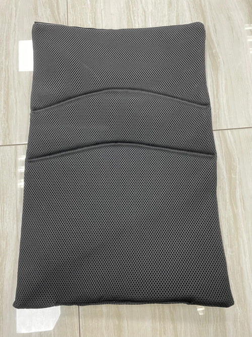 The Journey Air - Replacement Backrest, a black rectangular mesh cushion with curved stitching, lies flat on shiny beige tiles, designed specifically as a backrest replacement for the Journey wheelchair.