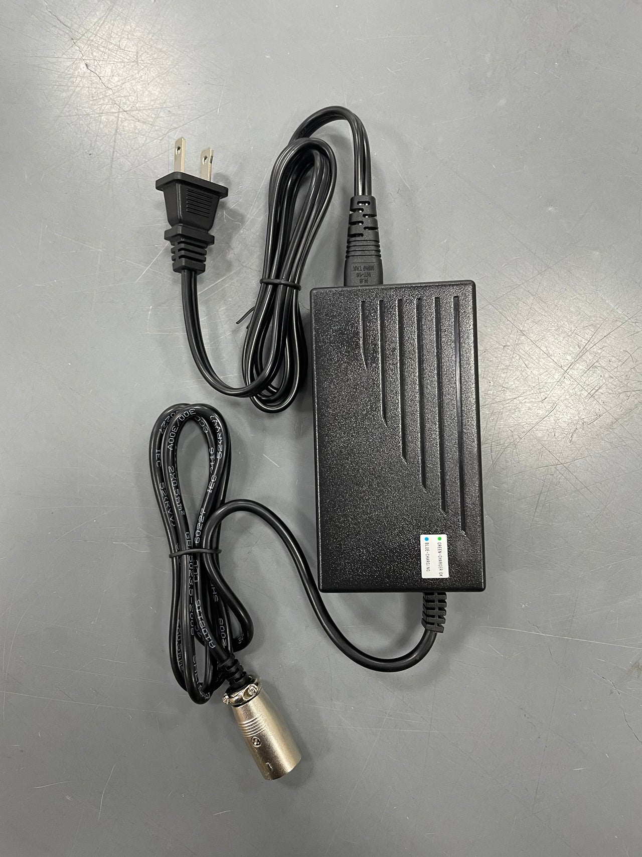 A Journey Air Elite - Replacement Charger in black with a two-pronged plug and detachable cable featuring a metal connector rests on a gray surface. It has a grooved design and labeled markings—perfect as a replacement charger.