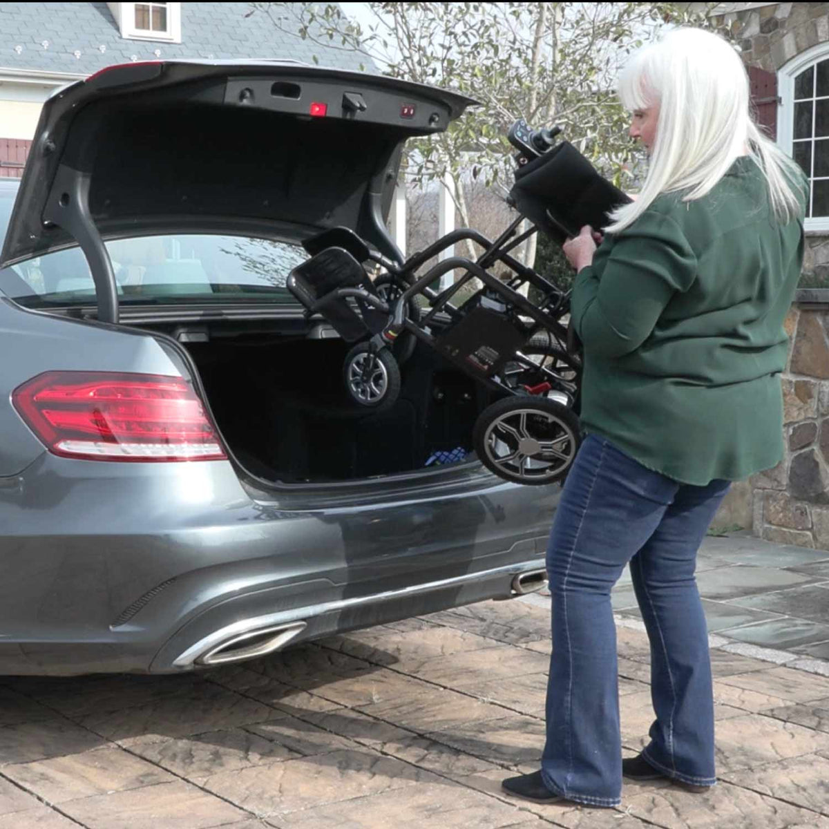 Person loading a Journey Air Elite Power Chair into the trunk of a car outside a house
