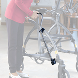 A person indoors holds a walker with a cane securely attached using the UPWalker® Cane/Umbrella Holder, keeping the cane suspended along the side of the walker for easy access.
