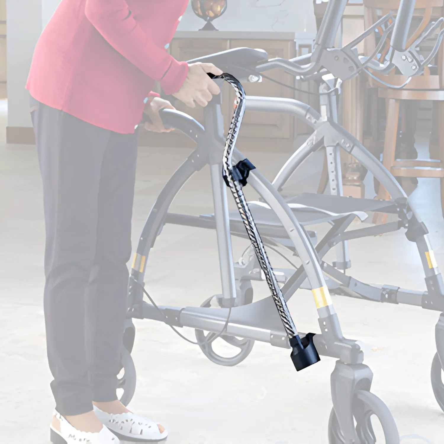 A person in a red top and dark pants holds a walker equipped with the Journey UPWalker Cane & Umbrella Holder, a hands-free accessory that securely grips and carries a cane or umbrella alongside the walker.