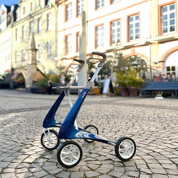 Blue Carbon Ultralight rollator on a cobblestone street with buildings in the background