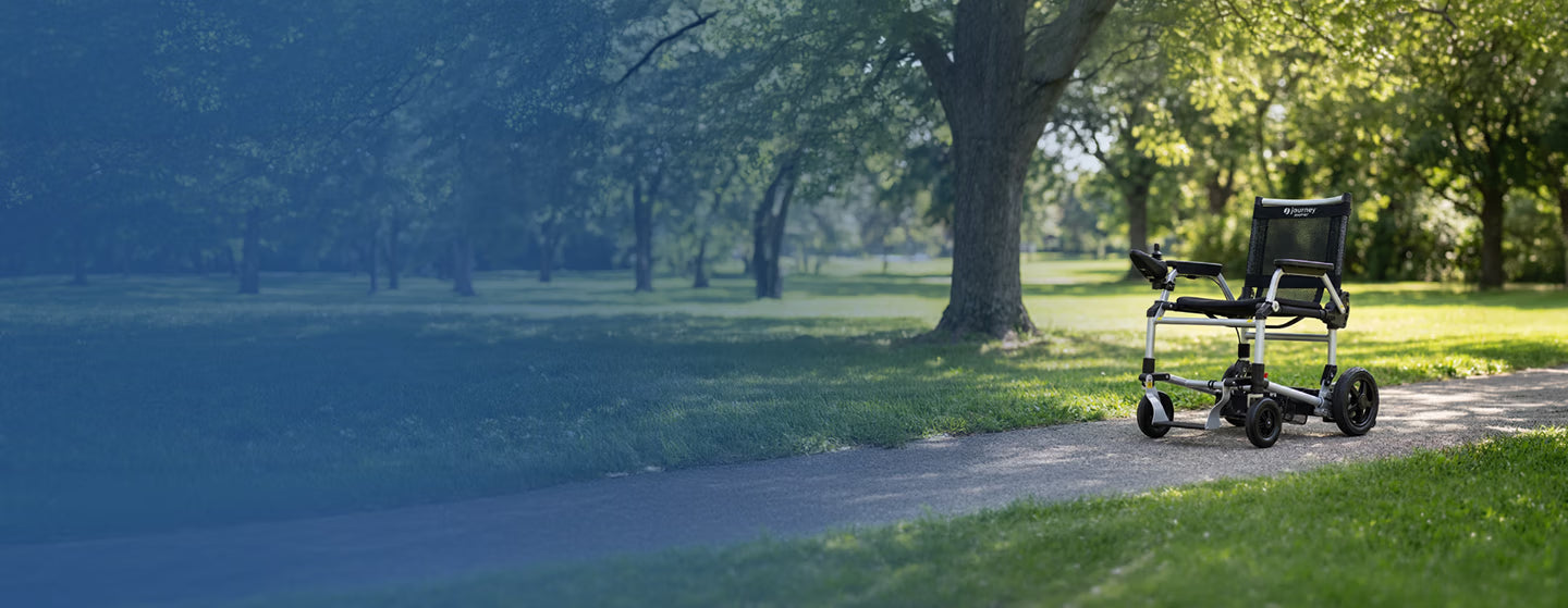 Journey Electric Wheelchair on a path in a park with trees and grass.