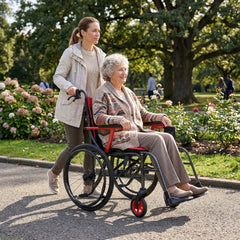 A young woman pushes an elderly woman in a Journey So Lite® C2 Ultra Lightweight Wheelchair through a park. Both are smiling and enjoying a sunny day, surrounded by trees and blooming flowers.