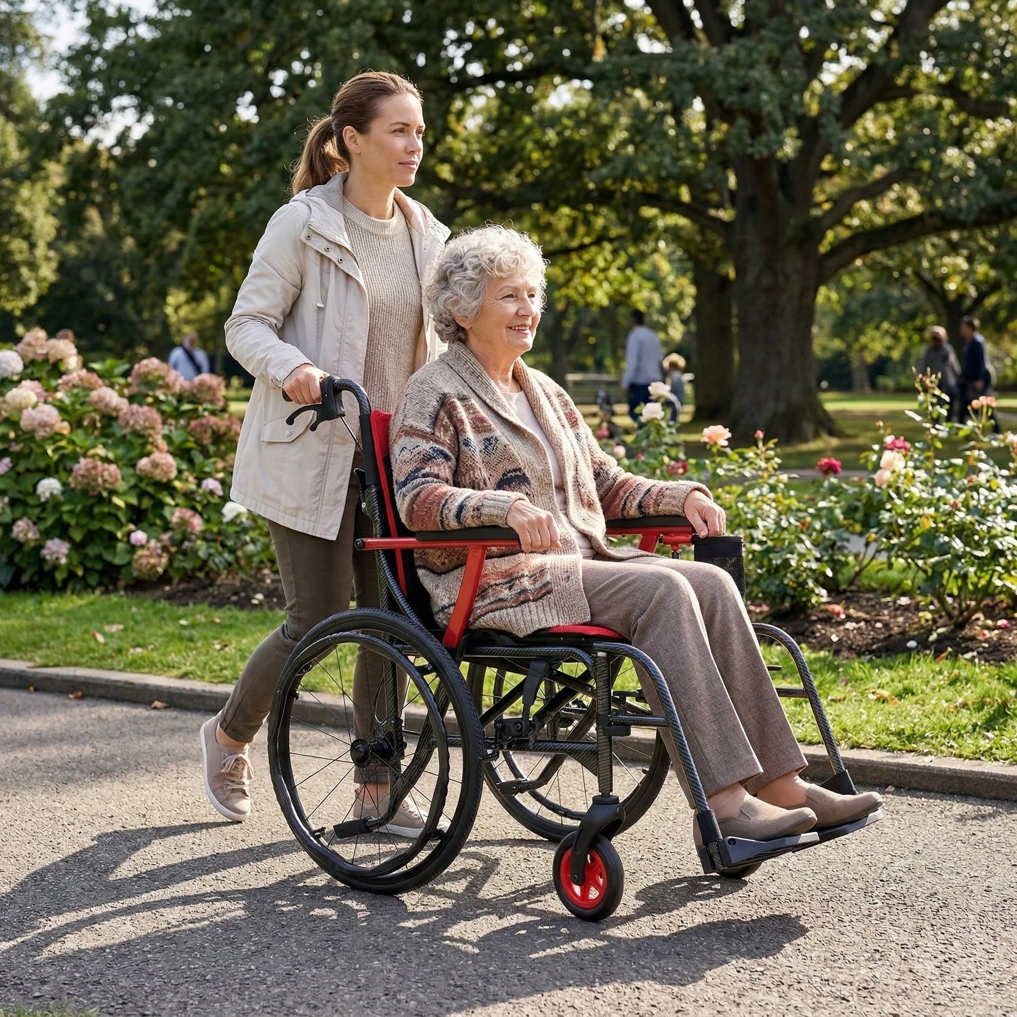 A young woman pushes an elderly woman in a Journey So Lite® C2 Ultra Lightweight Wheelchair through a park. Both are smiling and enjoying a sunny day, surrounded by trees and blooming flowers.