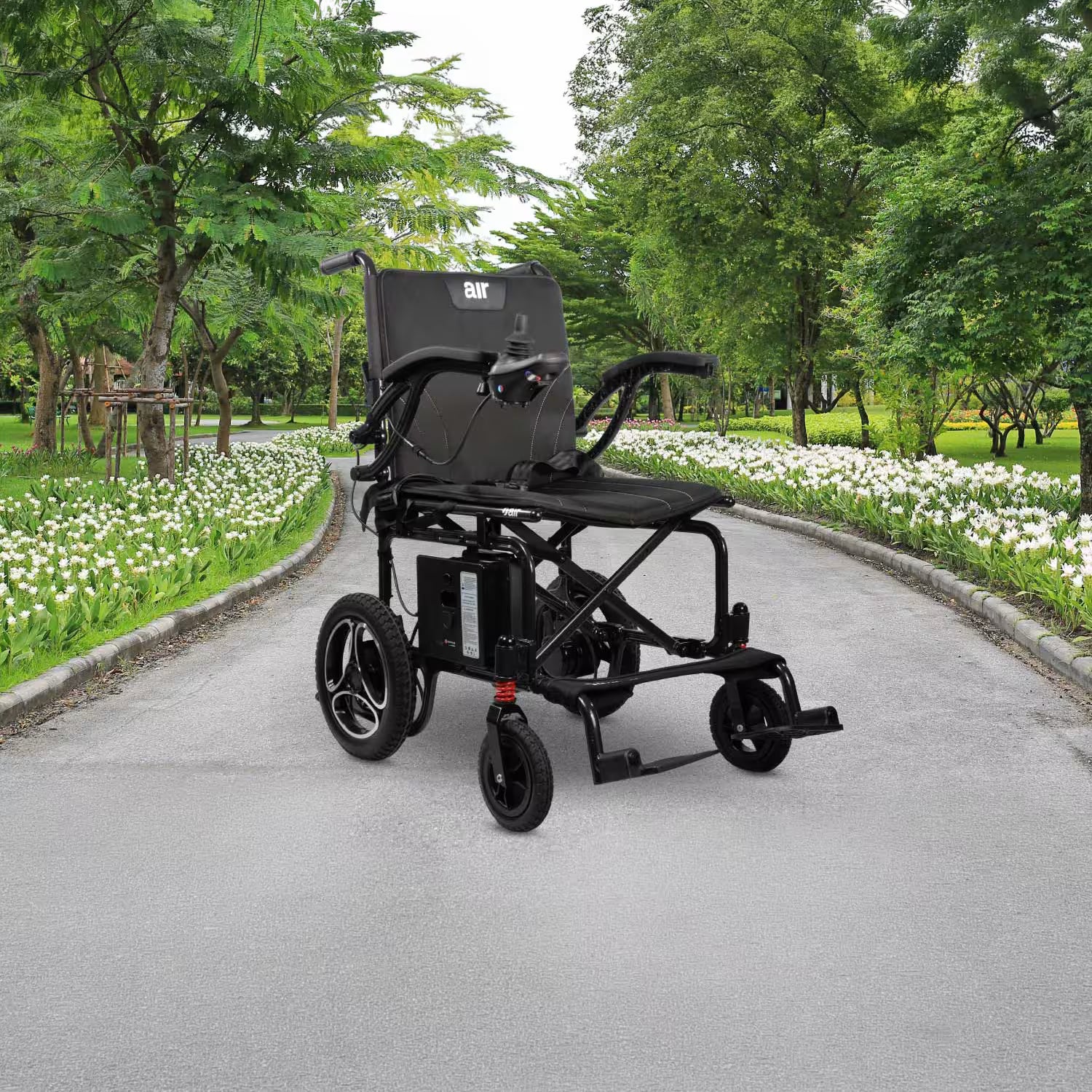 Journey Air 2026 portable folding electric power chair shown outdoors on a paved park path with green trees and white flowers, highlighting its travel-friendly design and 300lb weight capacity.