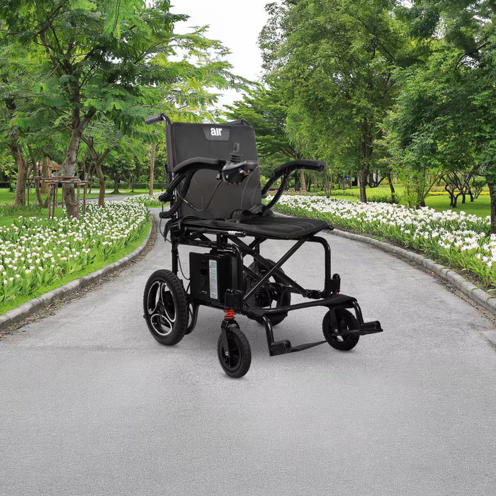 Journey Air 2026 portable folding electric power chair shown outdoors on a paved park path with green trees and white flowers, highlighting its travel-friendly design and 300lb weight capacity.