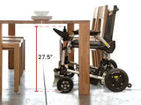 Journey Zoomer lightweight folding power chair positioned under a wooden dining table showing 27.5-inch clearance for comfortable dining use and accessibility in indoor settings.
