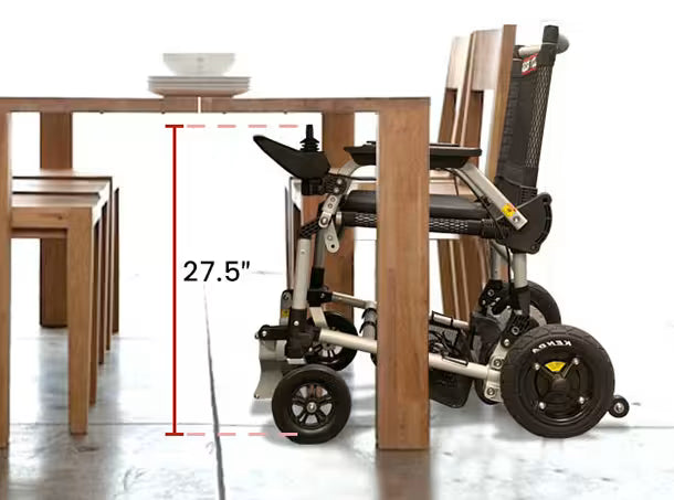 Journey Zoomer lightweight folding power chair positioned under a wooden dining table showing 27.5-inch clearance for comfortable dining use and accessibility in indoor settings.