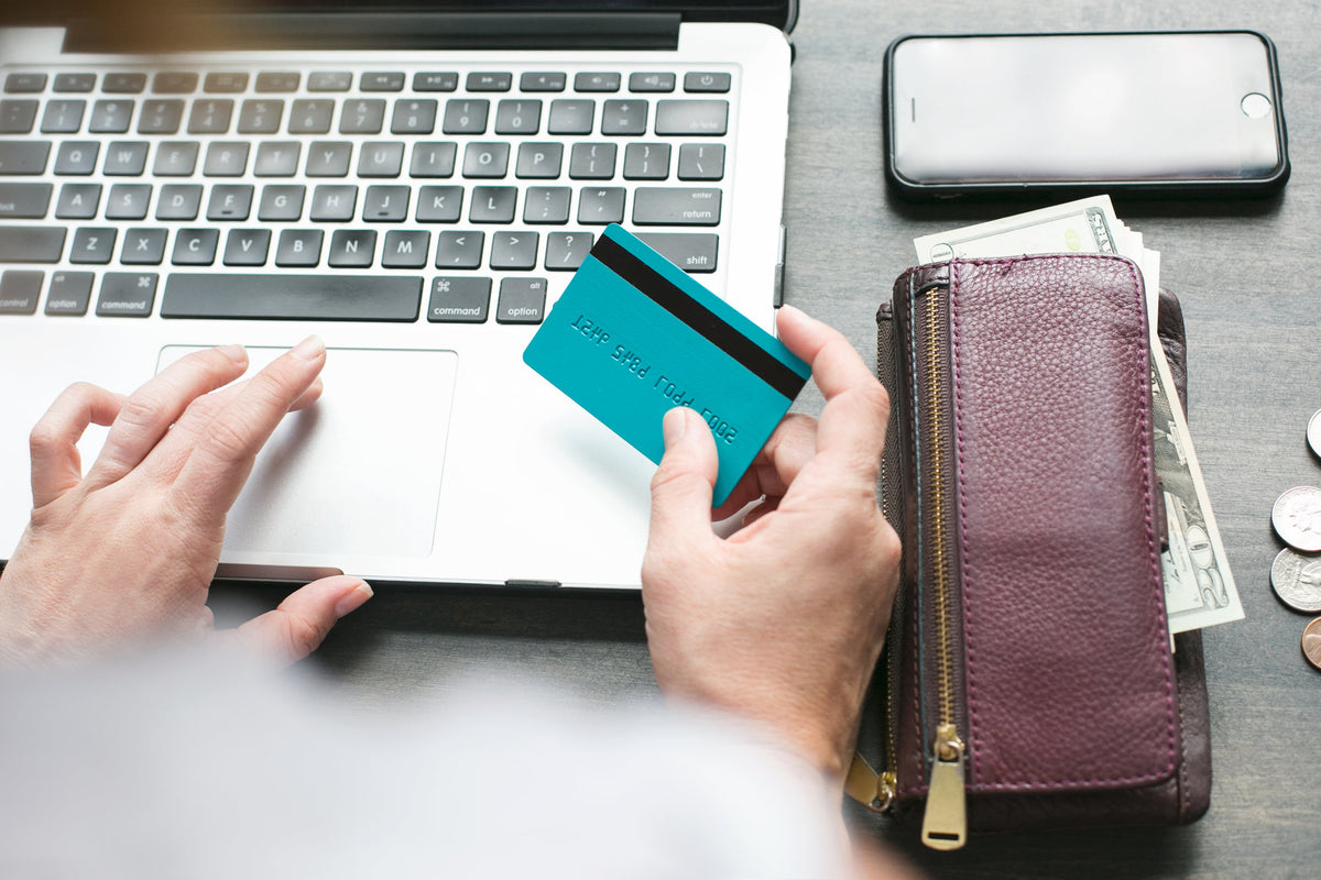 Person using a laptop with a teal card, wallet, and phone on a table.