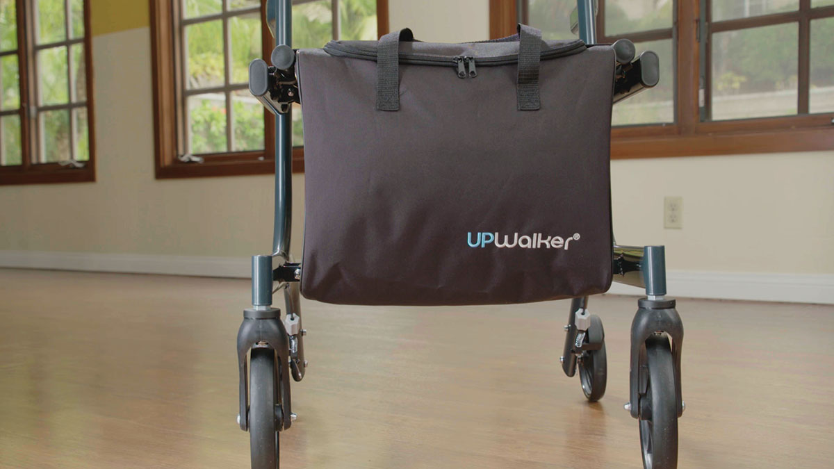 A close-up of an UPWalker with an UPWalker® Personal Item Bag, attached by Velcro straps, standing on a hardwood floor in a room with large windows.