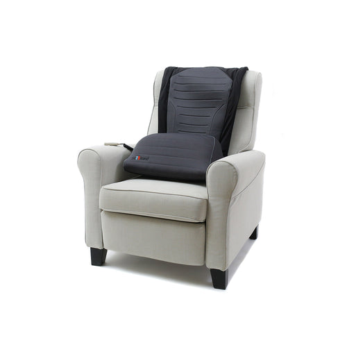A light beige upholstered armchair features the SitNStand Lift Assist Classic for Home—a black and gray portable lift assist cushion with a wired remote—draped over the backrest and seat.