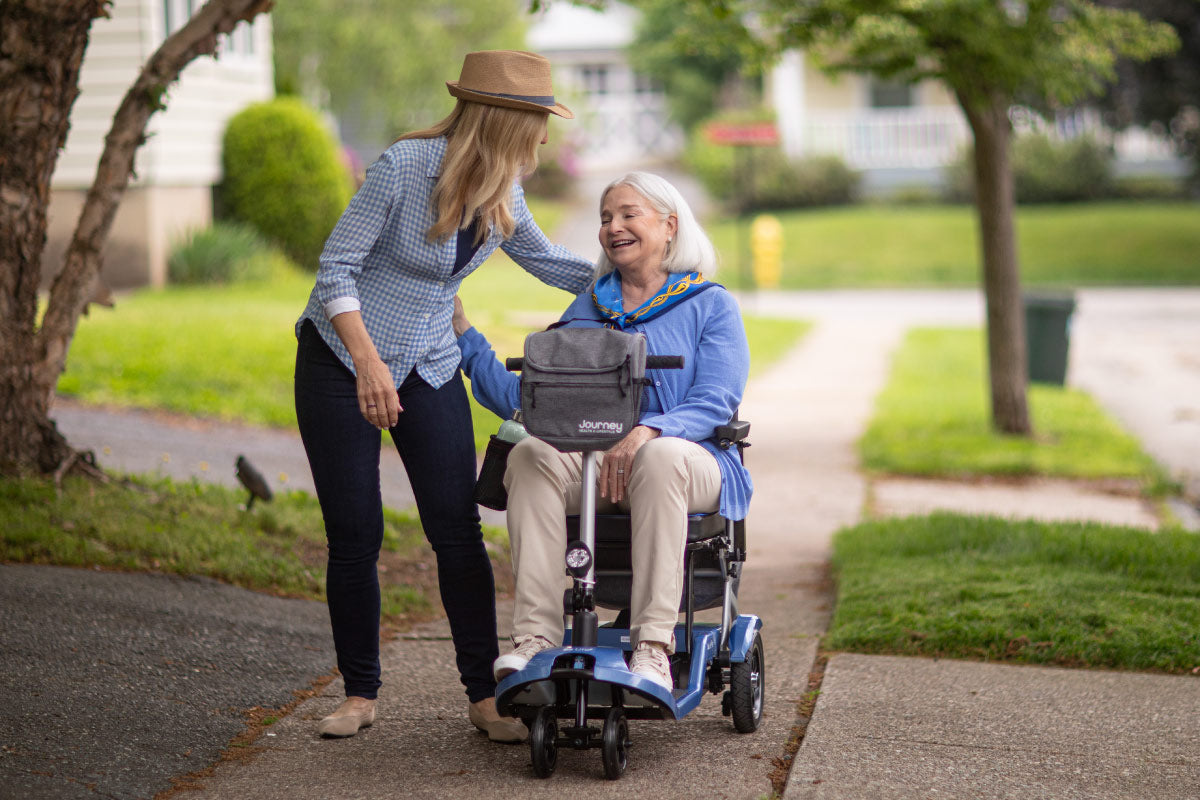 Woman walking with older woman riding a So Lite Scooter on a sidewalk