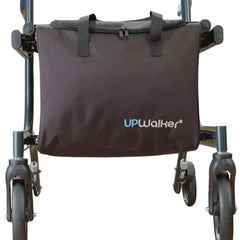 A close-up of the Journey UPWalker Personal Item Bag – Walker Accessory in black, attached to the front of a walker. The bag features top handles and a zipper for hands-free storage, with walker wheels and metal frame partly visible.