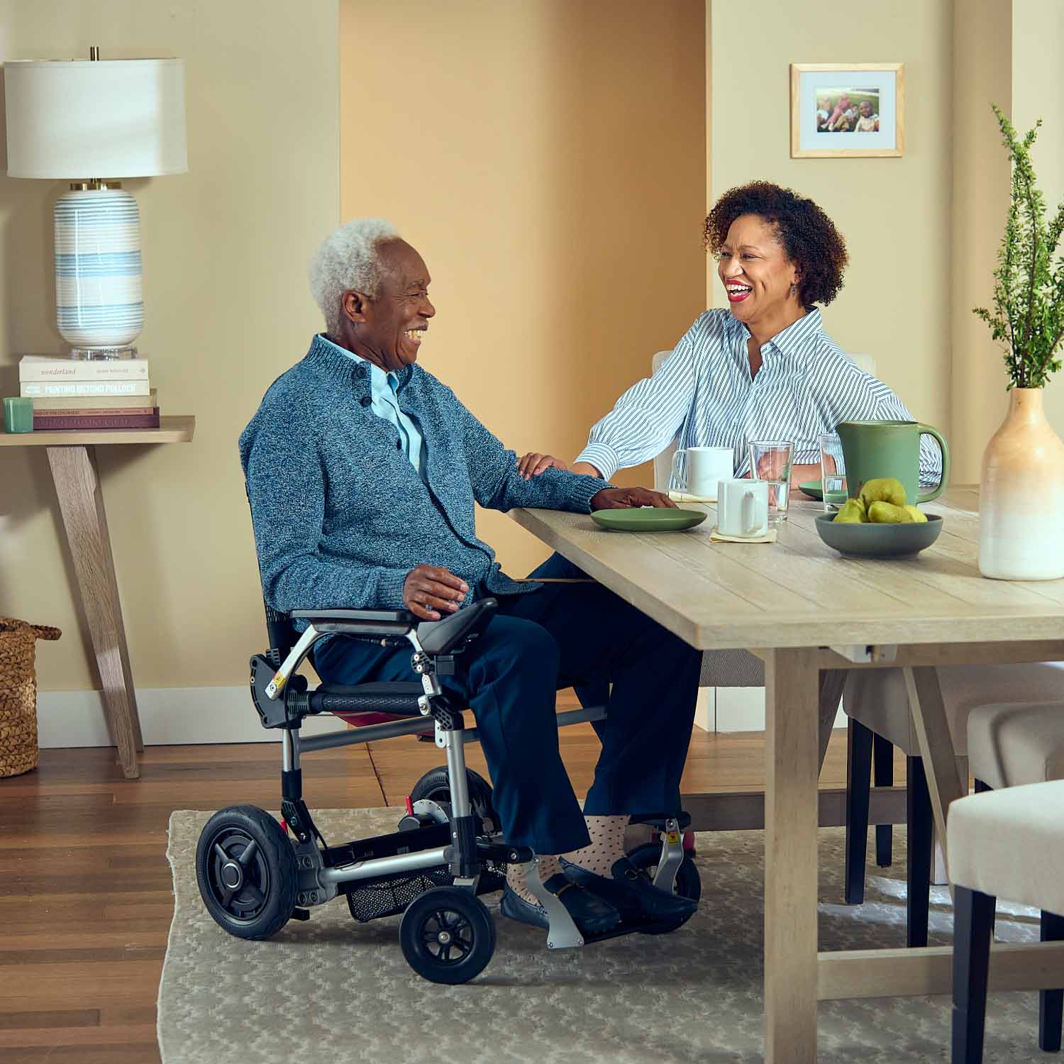 Man in a journey power chair  sitting at a dining table with a woman, both smiling.