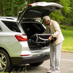 Man loading a power chair into the trunk of a car outdoors.
