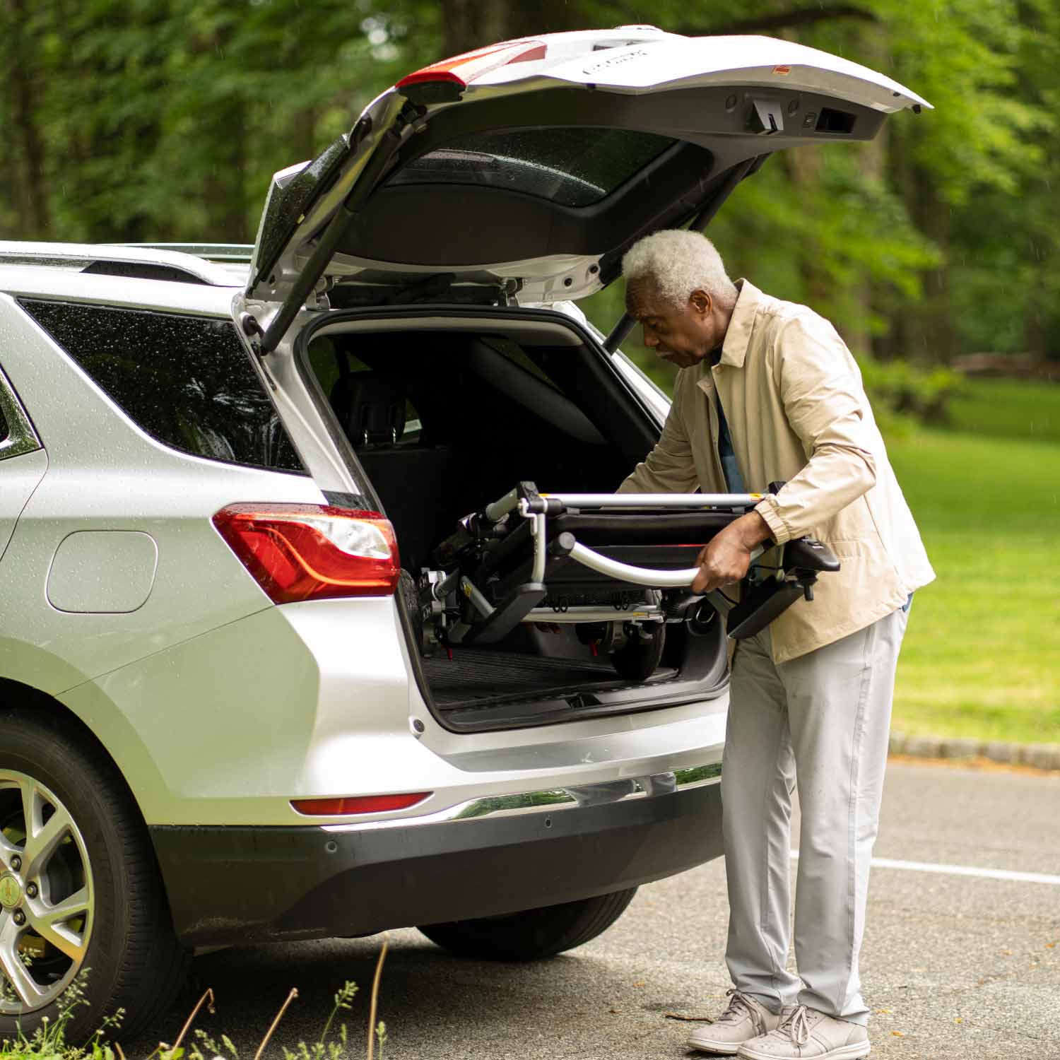 Man loading a power chair into the trunk of a car outdoors.